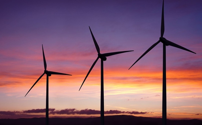 A scenic view of wind turbines at sunset, with the sky illuminated in warm colors of orange and purple.
