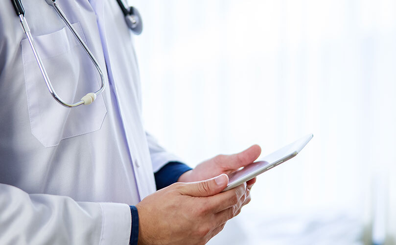 Henkilö lääketieteellisissä varusteissa pitelee tablettia käsissään