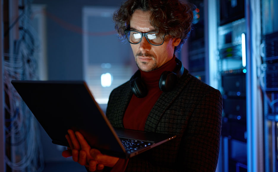 Man operating a laptop in a modern server room.