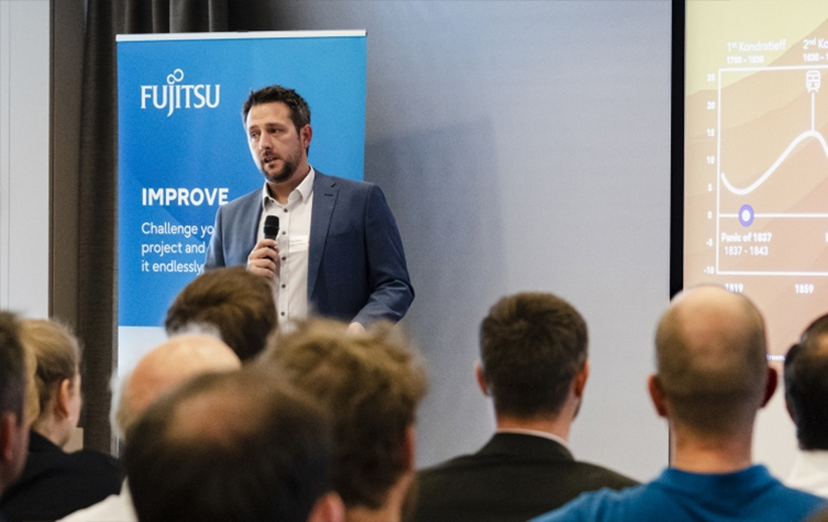 A man stands at a podium, delivering a presentation to an audience at a professional conference.