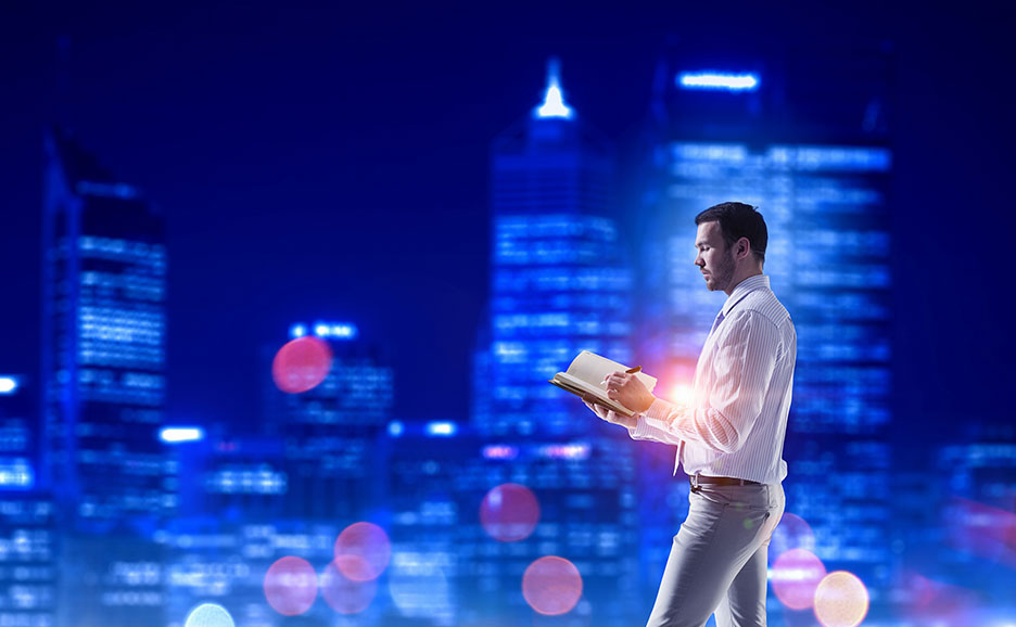 夜景を背景に、男性が手帳に書き込んでいる。