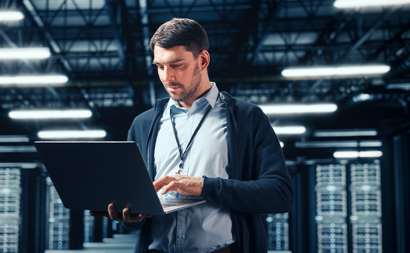 Technician using a laptop to monitor and manage servers in a modern data center