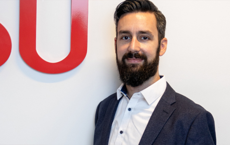 A bearded individual stands before a red and white sign