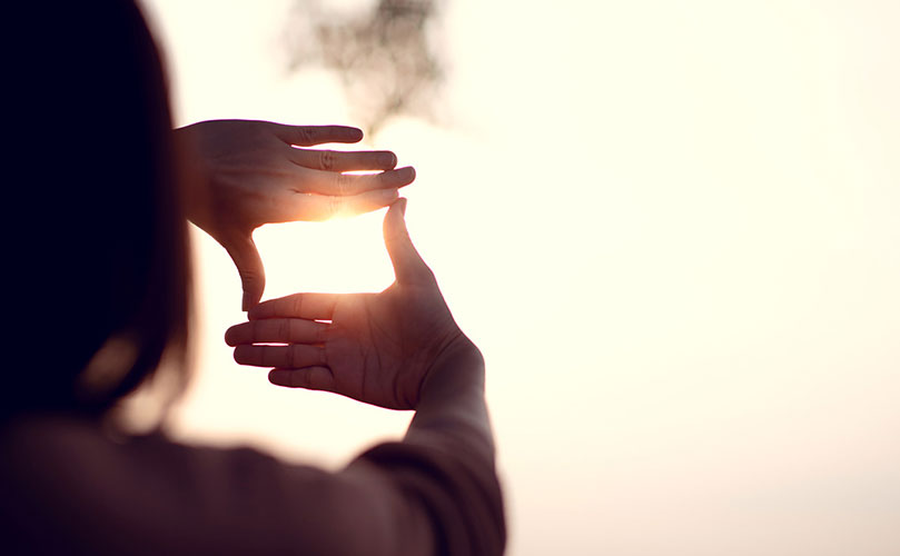 A person with their hands pointed to the sky, making a square, ensuring the sun is in the middle of the square