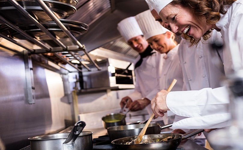 Três chefs numa cozinha a sorrir e a cozinhar