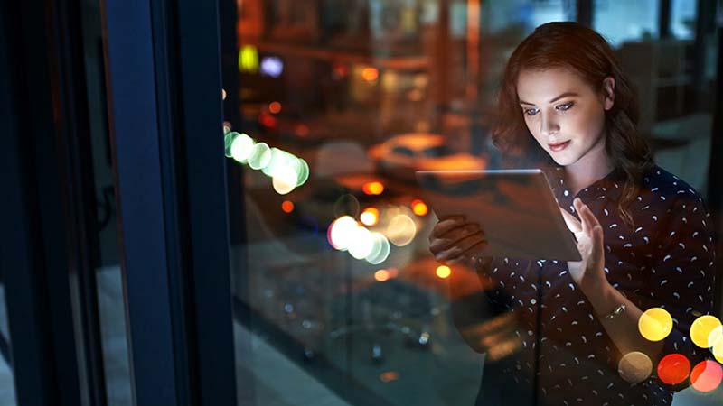 Une femme debout à côté d'une fenêtre regardant une tablette