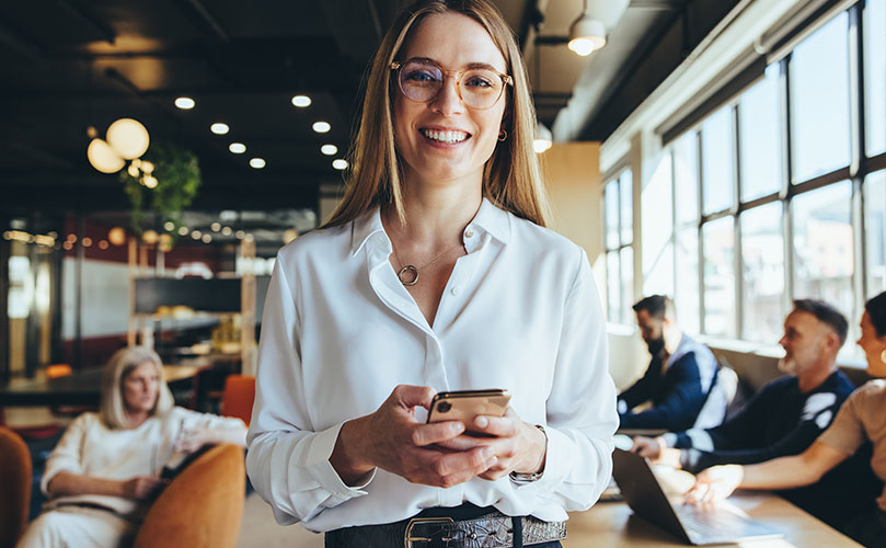 A professional woman in glasses using a cell phone in an office setting.