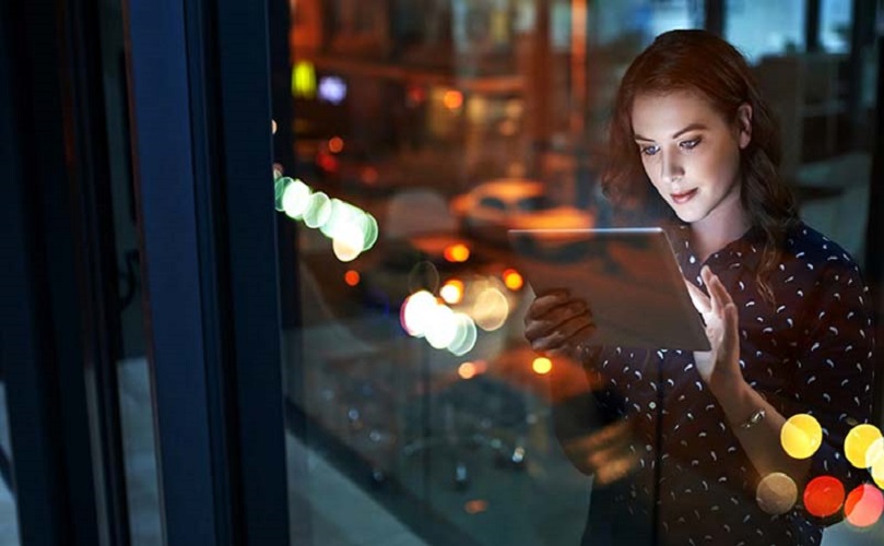 A woman standing next to a window looking at a tablet