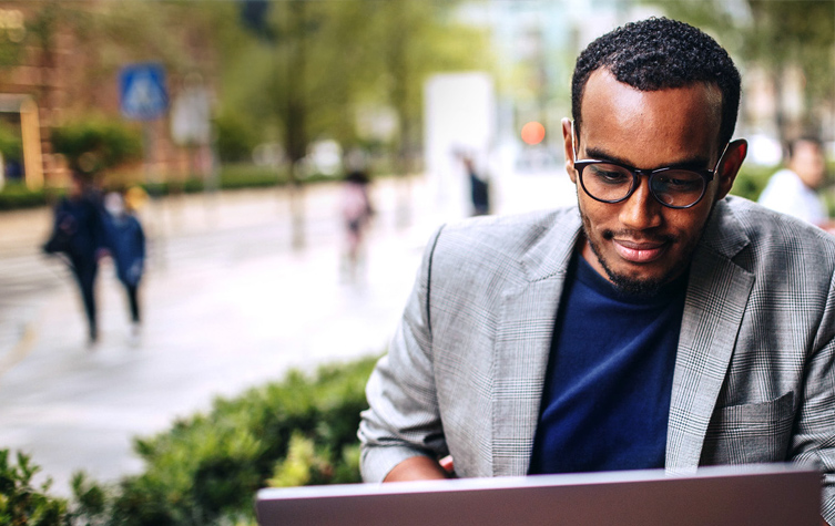 A man in glasses is observing his laptop