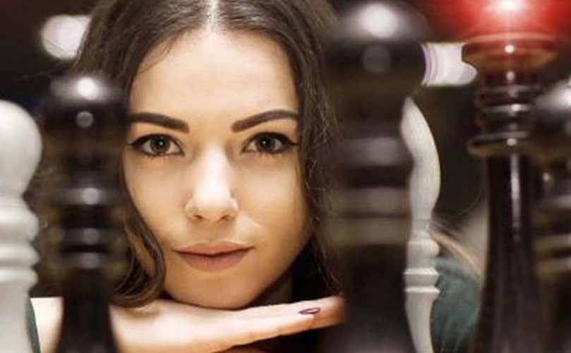 A woman looking at the camera with chess pieces in front of her