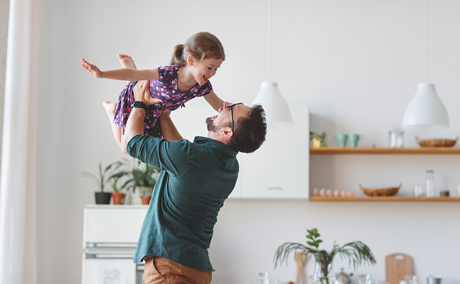 A father lifting his daughter high to play.