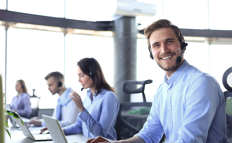 ヘッドセットを装着し、笑顔でカメラを見るコールセンター従業員。