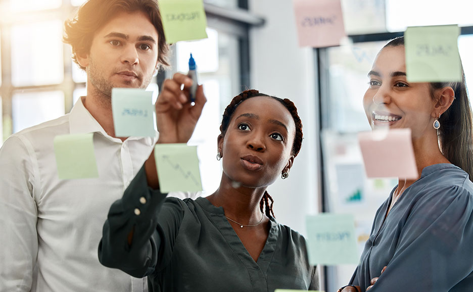クリアボードに張られた付箋,会議する若い３人の男女