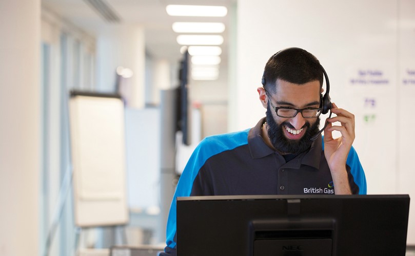 Un trabajador sonriendo a su ordenador mientras habla con su auricular