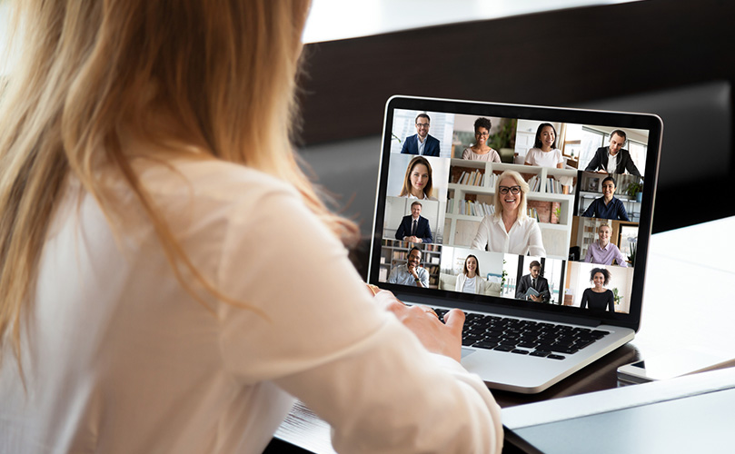 Le dos d'une femme sur son ordinateur dans lequel il est possible de voir une réunion virtuelle avec plusieurs autres personnes
