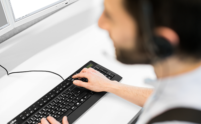 A man with a headset is engaged in typing on a computer keyboard, concentrating on his task.