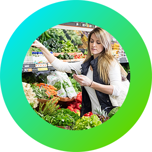 A woman selecting vegetables in a shop and looking at a mobile phone