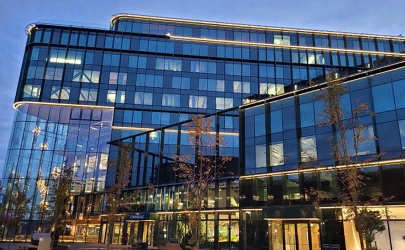 The exterior of a contemporary office building at dusk, featuring a striking design with glowing lights and darkening sky.