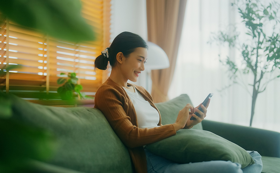 ソファに座ってスマートフォンを見ている若い女性