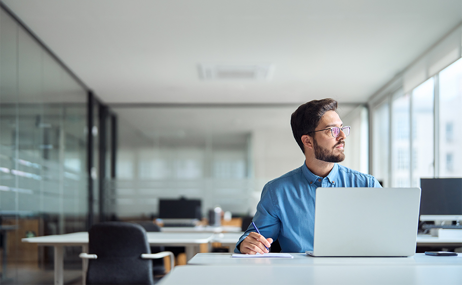 オフィスでPCを使用しながら、窓の外を眺める男性