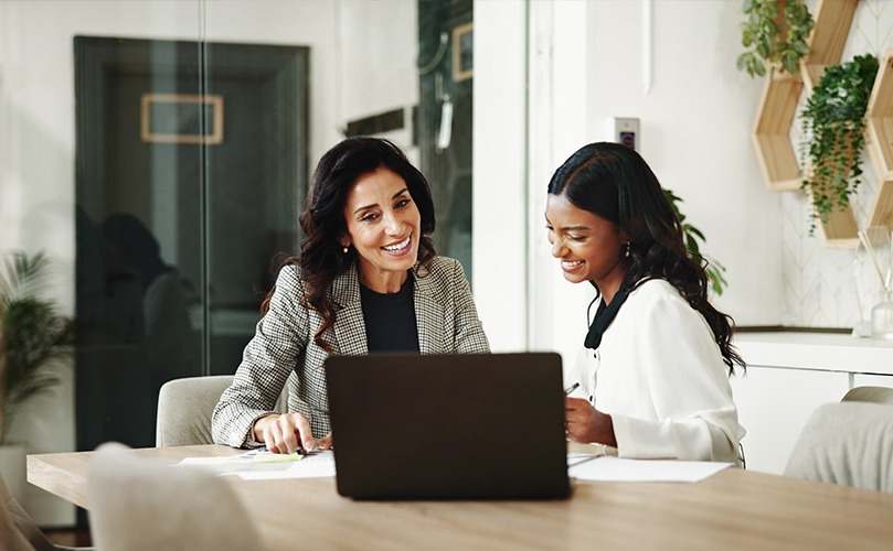 Two female colleagues looking at a laptop whilst sitting at a desk 