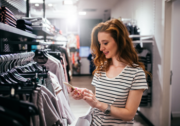 店舗でスマートフォンを操作しながら買い物を楽しむ女性の画像