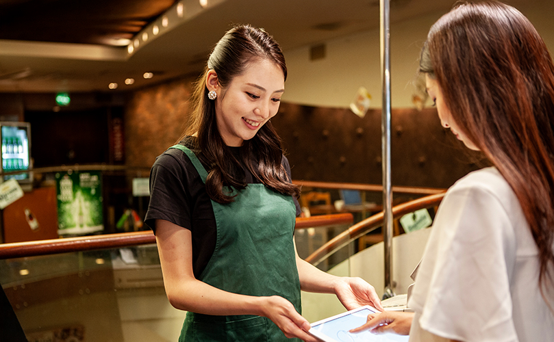 カフェで店員にタブレットを見せる女性客