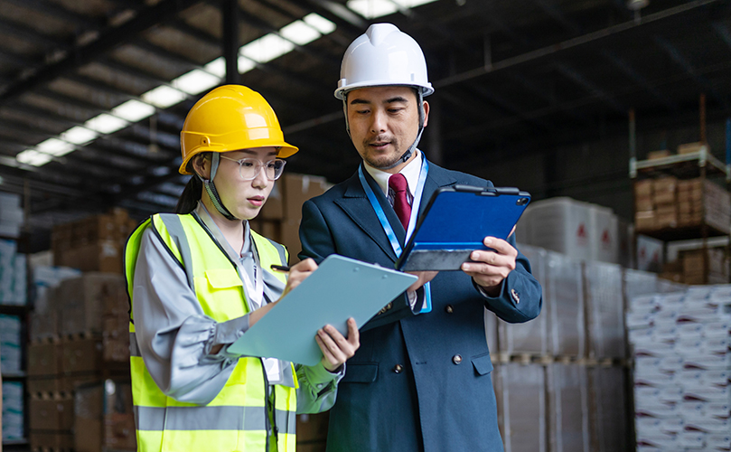 倉庫で働く人がタブレットと書類を確認している様子