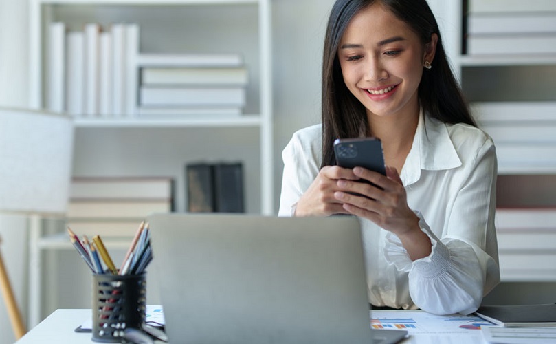 PCの前でスマートフォンを操作する女性