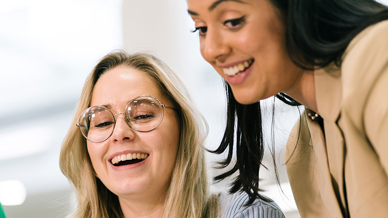 Dos mujeres mirando algo fuera de marco y riendo
