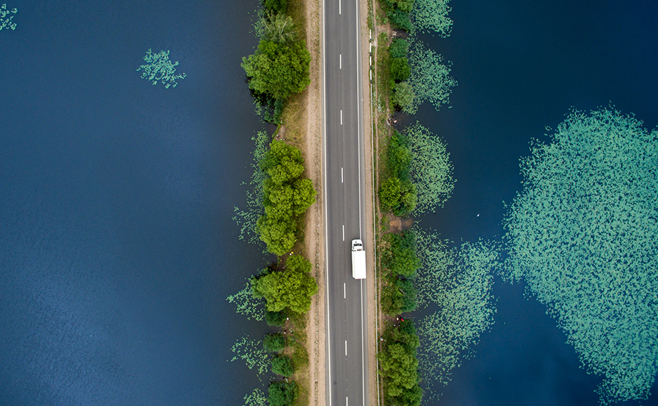 青い海の上を横切る、木々に囲まれた道路を上空から写したイメージ写真