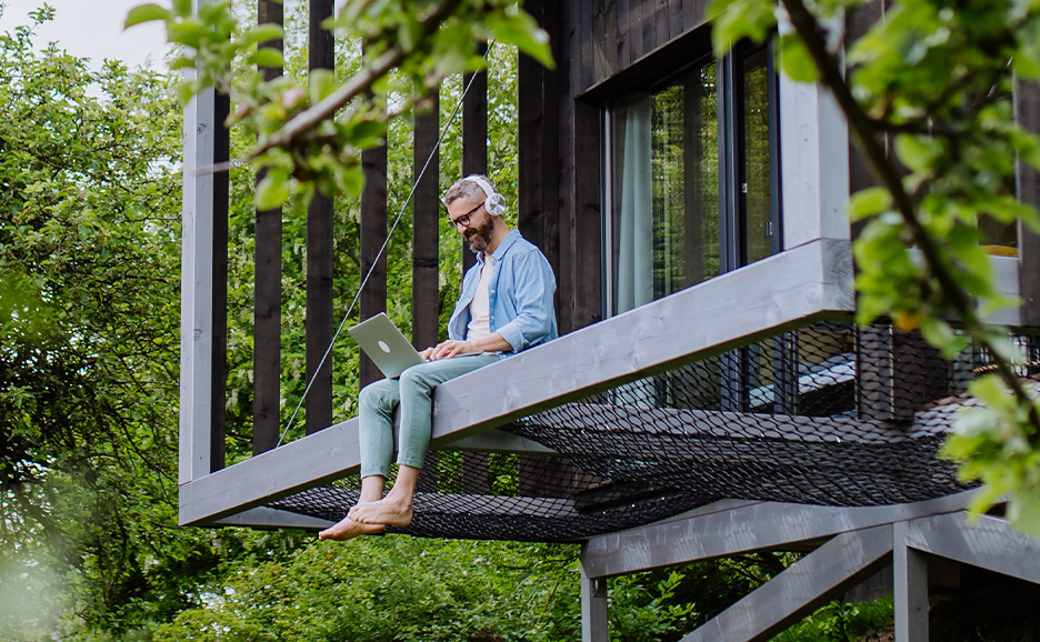 ヘッドフォンをした男性がツリーハウスの外、ノートパソコンで作業している写真