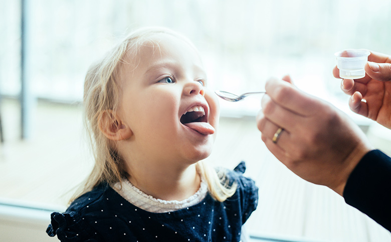 自宅で幼い娘に咳止めシロップを飲ませている母親の写真