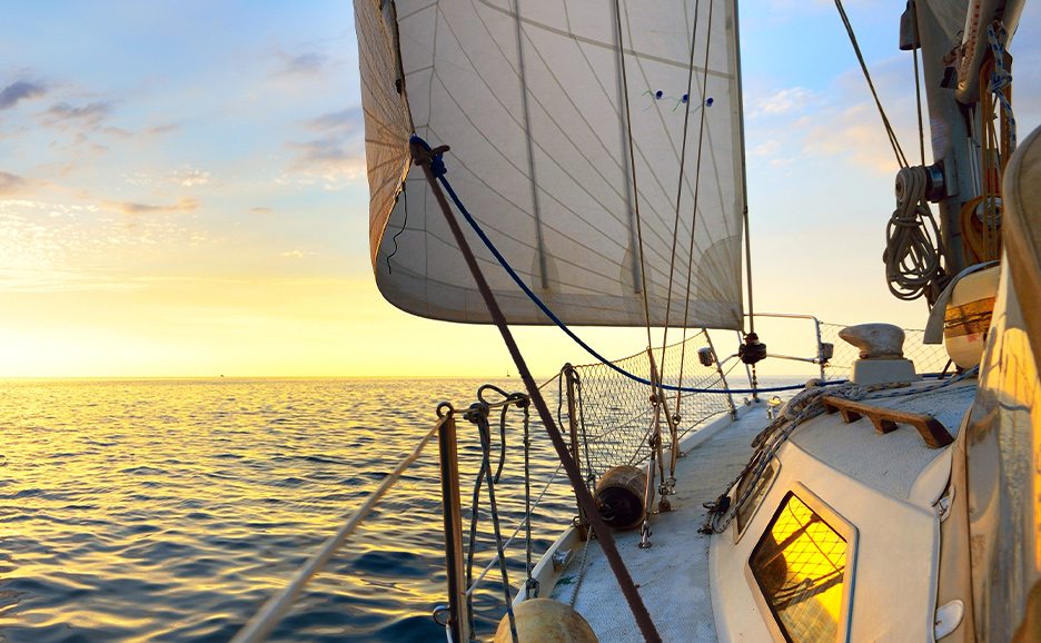 Segelboot auf offenem Meer bei Sonnenuntergang, ruhiges Wasser und klarer Himmel