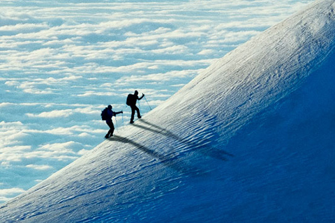 Zwei Bergsteiger besteigen einen verschneiten Hang über den Wolken