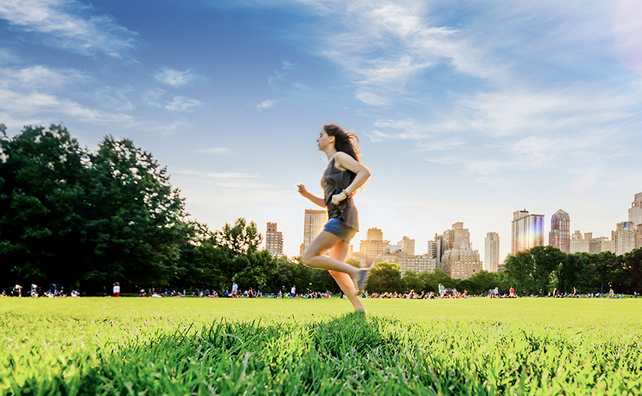 A woman running in a park with a city skyline in the background.