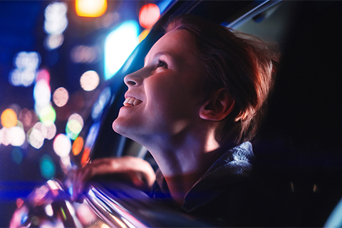 uma criança a olhar pela janela de um carro numa noite néon