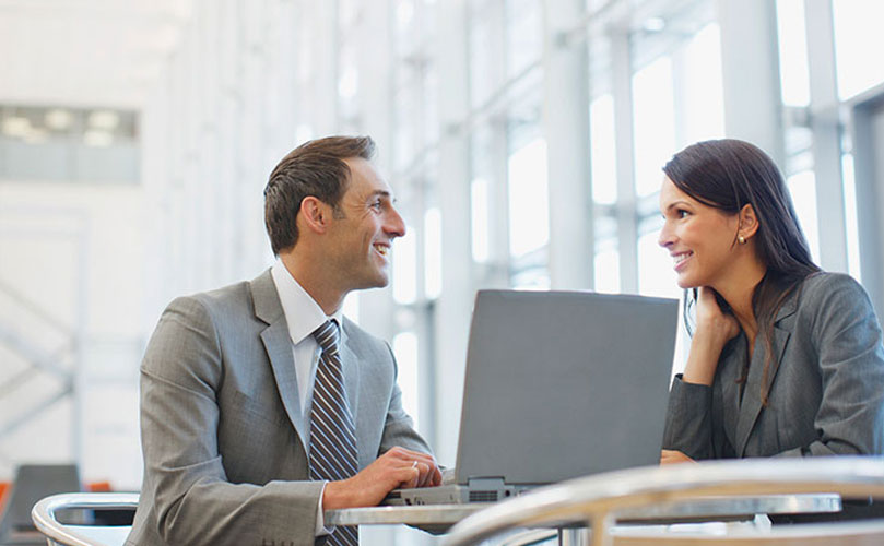 A man and woman in business attire sitting at a table with a laptop.