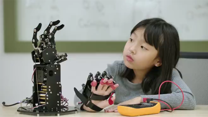 Young girl looking at a robotic arm depicting digital healthcare platform experts
