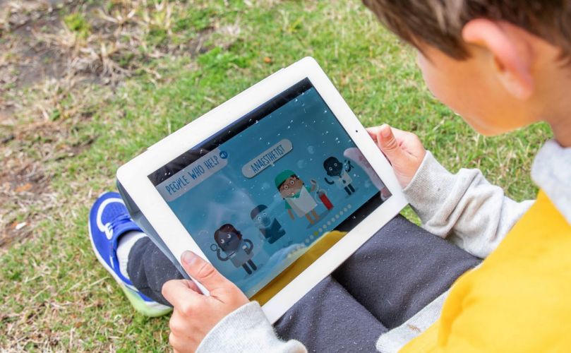 A child sitting on grass playing a game on a tablet