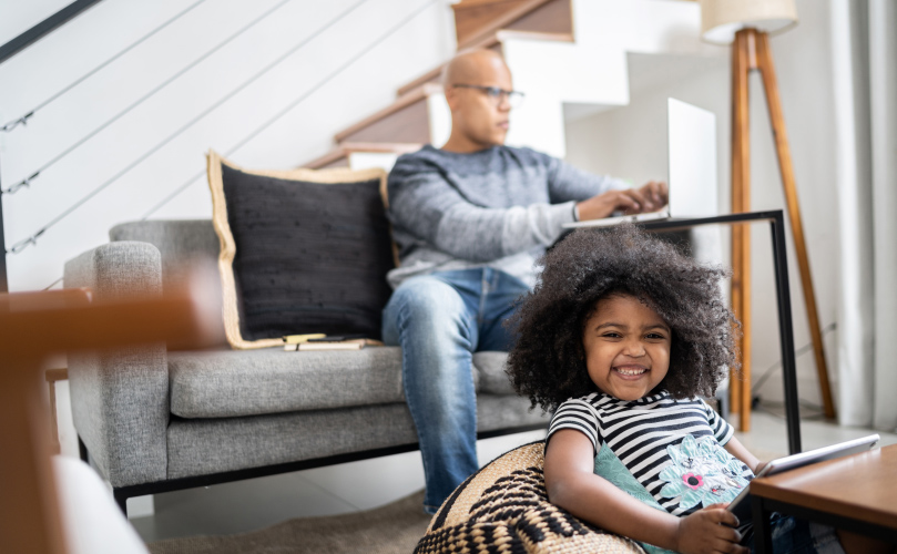 A picture of a child laughing with a blurred background of an adult working on a computer