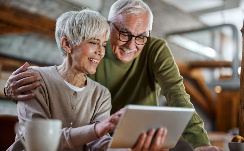 Two senior people laughing and looking at a tablet