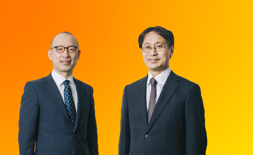 兩個男人微笑著看著鏡頭,背景是橙色的