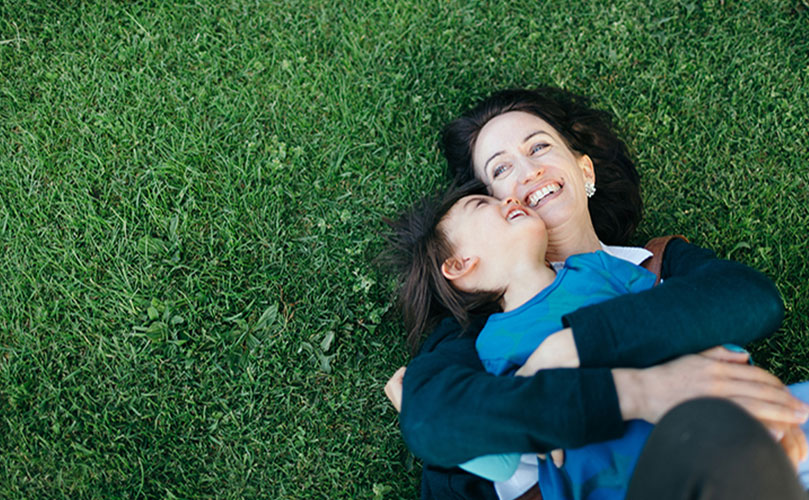 Seorang wanita memeluk seorang anak sementara keduanya berbaring di rumput