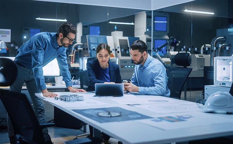 A team of three working together on a laptop in a bright office environment.