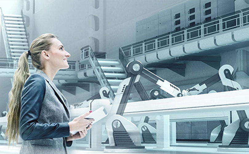 A professional woman in a grey jacket stands in a futuristic factory, with robotic arms working on a manufacturing assembly line in front of her.