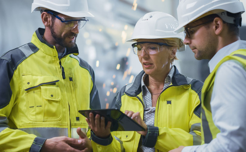 A woman and two men wearing protective gear looking at a tablet