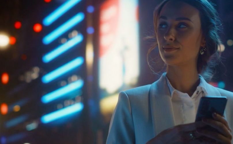 一位女士拿著電話,看著身後明亮的城市燈光