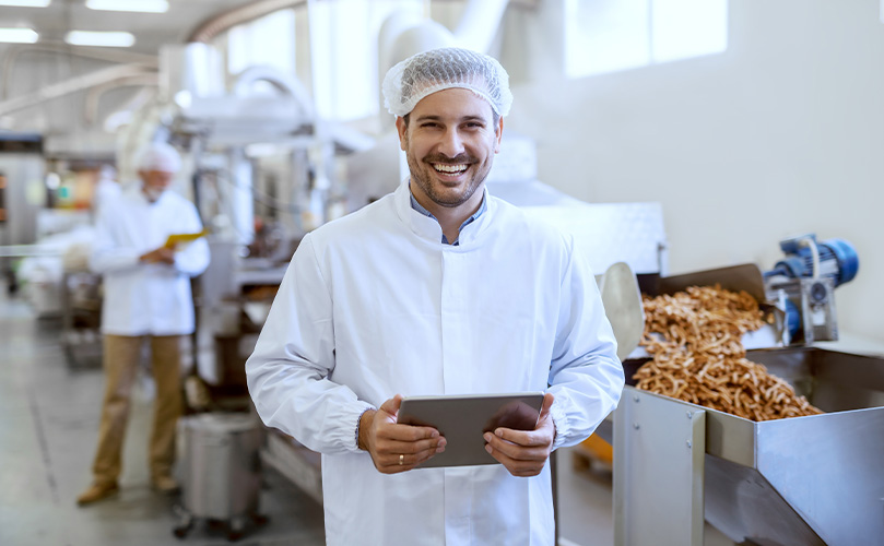 A man in a kitchen cap smiling with a tablet in his hand