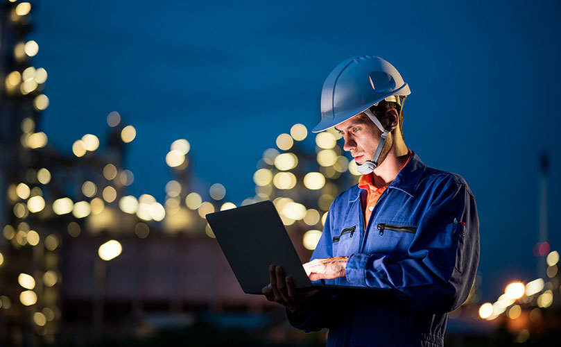 Ingenieur in Arbeitskleidung prüft Daten auf Laptop im Industriegebiet